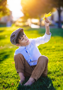 young child sitting in the grass outside holding a leaf in the air, outdoor photography, outdoor photographer, portrait photography, portrait photographer