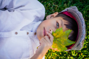young child laying in the grass holding a leaf over his eye, outdoor photographer, portrait photographer, outdoor photography, portrait photography